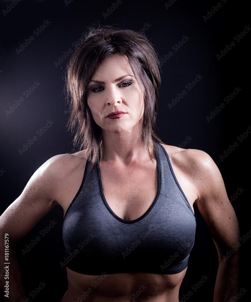 Studio vertical portrait of one female fitness model on black background.  Showing off great muscle tone in biceps, chest, triceps. Black sports top  bra, black hair, red lipstick Stock Photo