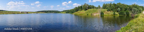 The hilly coast of the lake with trees and meadows, a place to relax on a summer day. panorama
