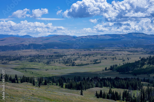 Fototapeta Naklejka Na Ścianę i Meble -  Valley in Yellowstone showing green field and mountains in the distance under puffy clouds casting shadows