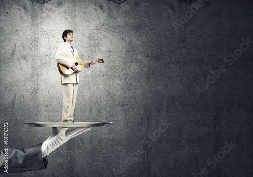 Businessman on metal tray playing acoustic guitar against concrete wall background