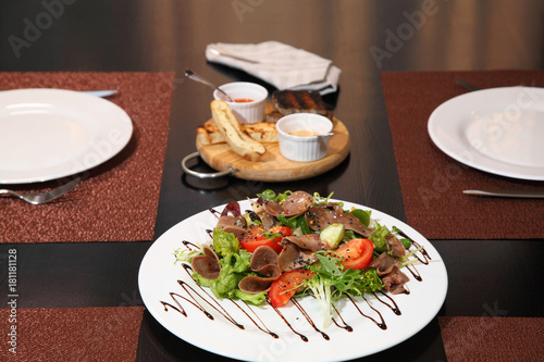 Salad with beef tongue with vegetables and herbs, dressed with sauce on a white plate.