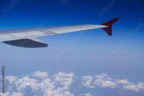 Wing of an airplane flying above the clouds with clear and sky as seen through window of an aircraft. Aerial view from airplane window for using air transport to travel.