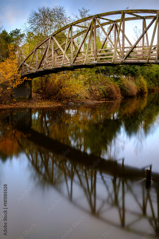 Fall colors and a bridge reflect on a quiet river