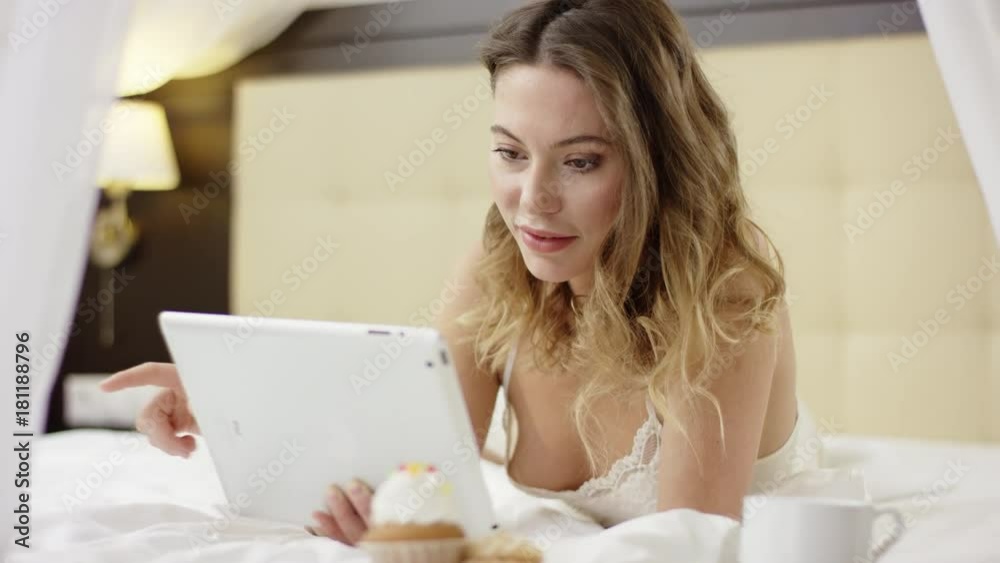 Attractive woman watching video on her tablet pc while lying near with cup of coffee and cupcake Attractive woman watching video on her tablet pc while lying near with cup of coffee and cupcake