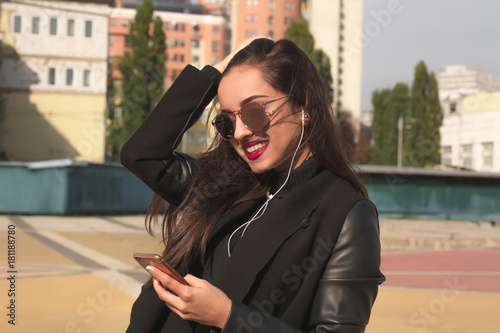 Lovely smiling model in glasses listen music on mobile telephone, standing at the street © vpavlyuk