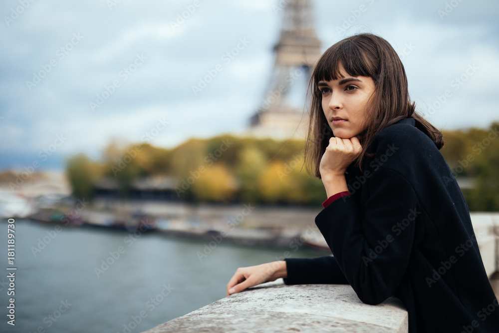 Beautiful young Parisian woman in long coat near the Eiffel tower on a autumn day