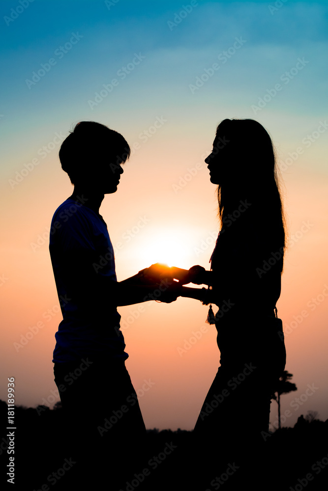 silhouette of a couple lovers standing holding hand at the sunset time and they gaze into each other’s eyes. Have a beauty pink and blue sky.