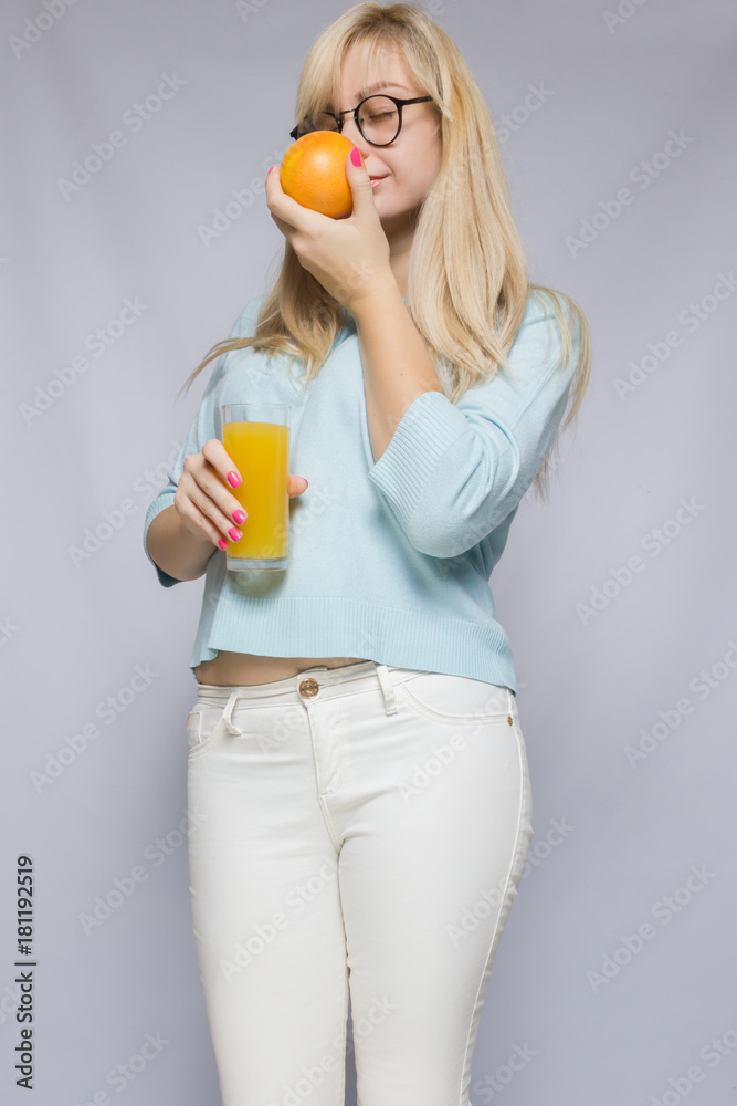 Portrait of a beautiful young blond woman with a glass of orange juice. Girl drinks juice and shows orange. Portrait of a beautiful young blond woman with a glass of orange juice. Girl drinks juice and shows orange.