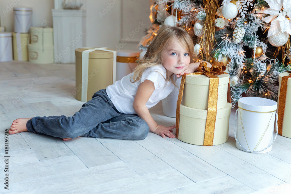 Naklejka premium Young girl opens a gift under a Christmas tree