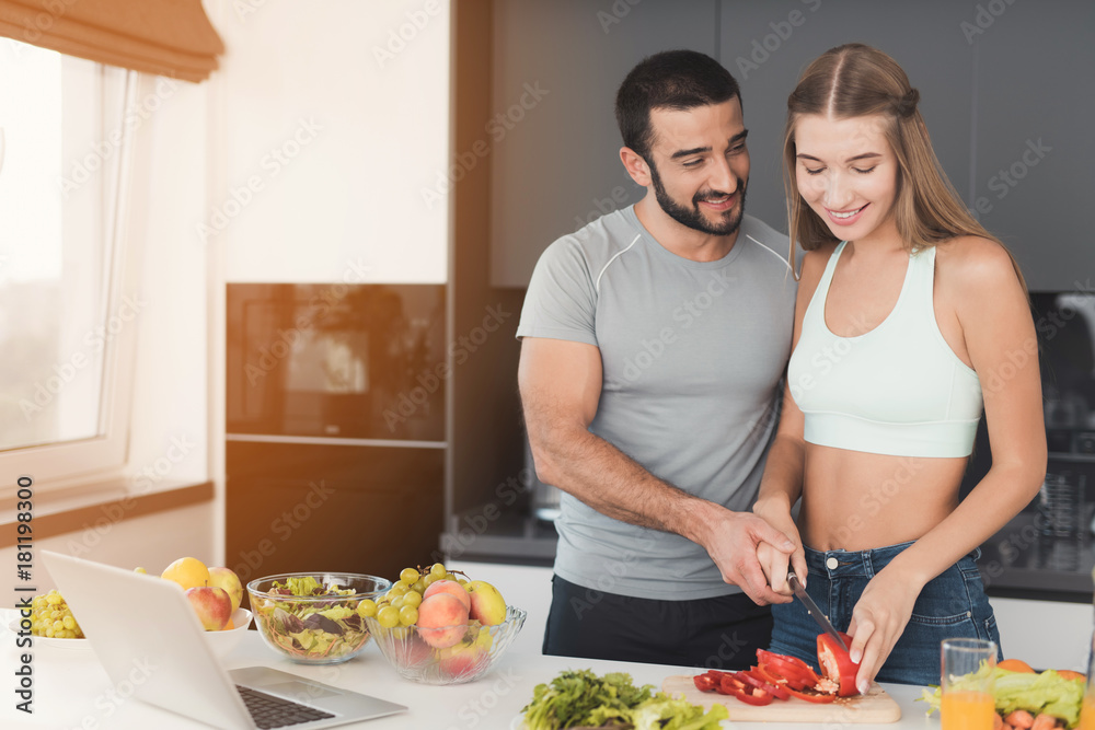 A couple is preparing a salad for breakfast. A girl cuts vegetables for a salad and a man helps her. A couple is preparing a salad for breakfast. A girl cuts vegetables for a salad and a man helps her.