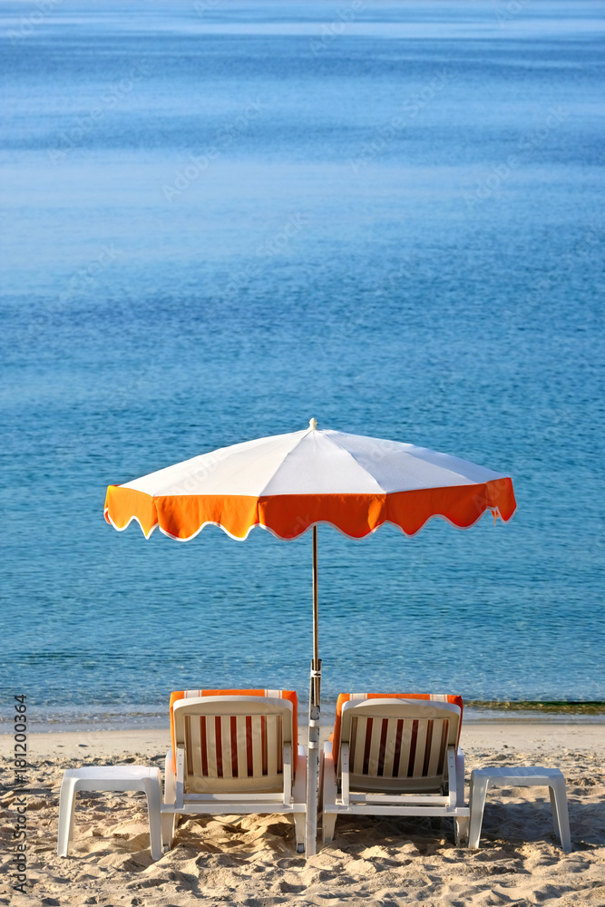 Fototapeta premium Luxury tropical caribbean beach resort sunbathing umbrella and lounger chair on sand deep blue sea summer holiday vacation photo vertical