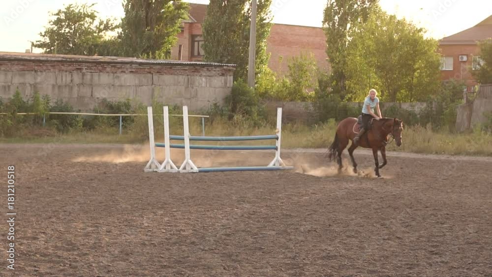 Professional rider on a horse jumps over a barrier. Competitive rider training jumping over obstacles at sunset. Mare jumps over barriers in training at the racetrack. Slow motion. Professional rider on a horse jumps over a barrier. Competitive rider training jumping over obstacles at sunset. Mare jumps over barriers in training at the racetrack. Slow motion.