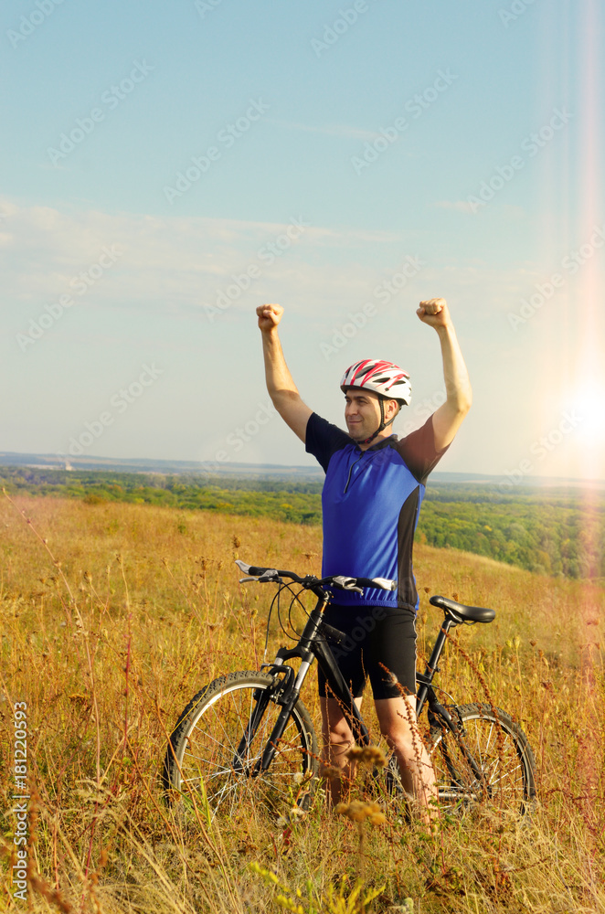 Mid age Male cyclist shows raised up hands gesture on the top of the hill Mid age Male cyclist shows raised up hands gesture on the top of the hill