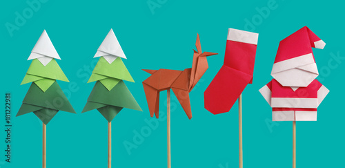 Handmade origami paper craft Santa Claus, green Christmas trees and reindeer on light green background