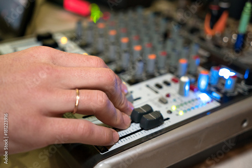 DJ working on a audiomixer at a nightclub. Close-up of hands adjusting quality of music using a knobs of the audio mixer
