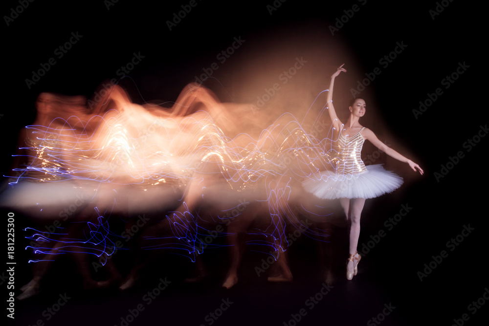 Fototapeta premium Young female / woman / girl ballerina in a white pack / tutu solo dancing doing stand on toes and leaves light leak trail of silhouette in black scene with reflecting floor and dark background