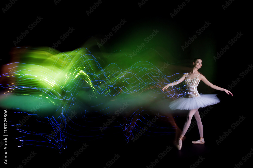 Obraz premium Young female / woman / girl ballerina in a white pack / tutu solo dancing and leaves green light leak trail of silhouette in black scene with reflecting floor and dark background