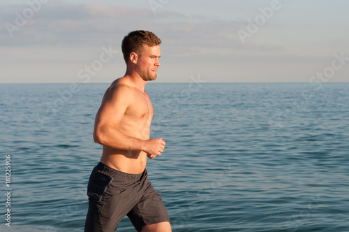 Muscular man barefoot running on beach