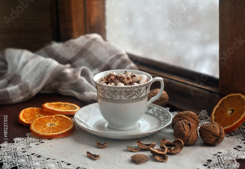 A cup of coffee with a marshmallow on an old wooden snow-covered window. Still life. Christmas and New Year card.