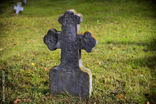 Old, stone, tombstone cross on a background of green grass.