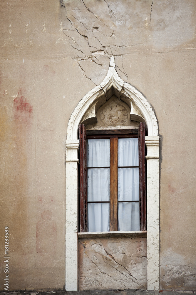 Withered facade with window of an old Italian town house. Cracks in the wall. Byzantine frame.