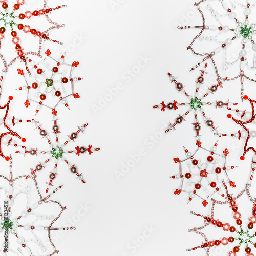 Christmas or winter concept. Frame of various handmade red green snowflakes made from beads and bugle on white desk background, top view. Layout for greeting card and winter holidays