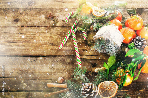 Magic Christmas background - vintage wood, candy cane, house, cinnamon, star anise, sweet mandarins with green leaves, cones, snowflakes. New Year. Top view, copy space, snow, bokeh.