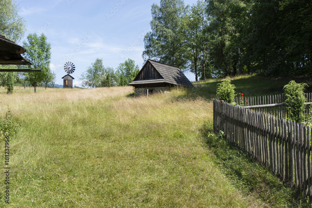 Wooden old fence with meadow, building and windmill in the background.