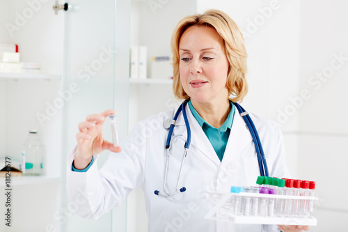 Blond nurse looking at one of flasks with sample of new vaccine