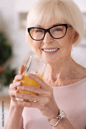 Close up of a cheerful senior woman drinking orange juice
