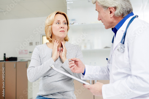 Sick mid-aged female complaining about sore throat to her doctor