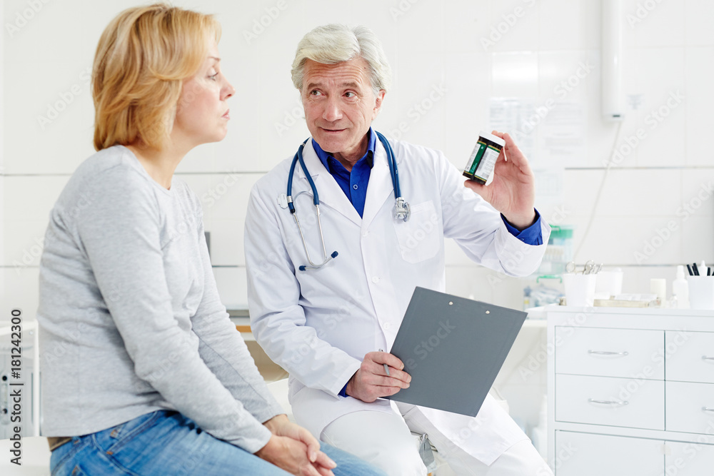 Mature clinician telling his patient about new pills and showing her pill-bottle