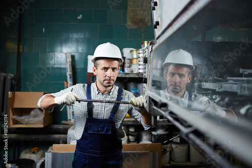 Worker in overall and harhat repairing industrial equipment photo