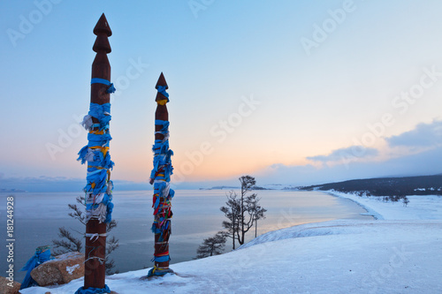 Lake Baikal in December. Olkhon Island on an early cold morning. Colored tapes on the acred pillars. View on the snow-covered sandy beach of the Sarayskiy Bay