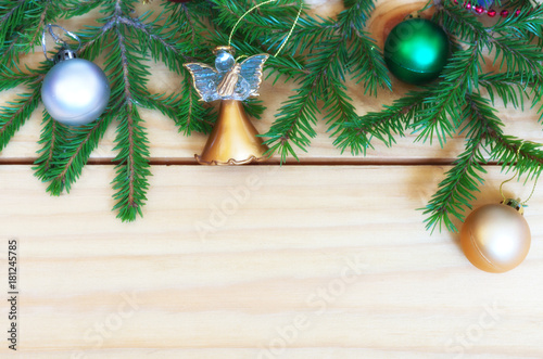 Christmas toy angel, shiny balls and green tree branches over a wooden background for congratulations