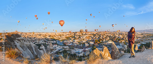 Fotografie A tourist girl on a mountain top enjoying wonderful view of the sunrise and balloons in Cappadocia