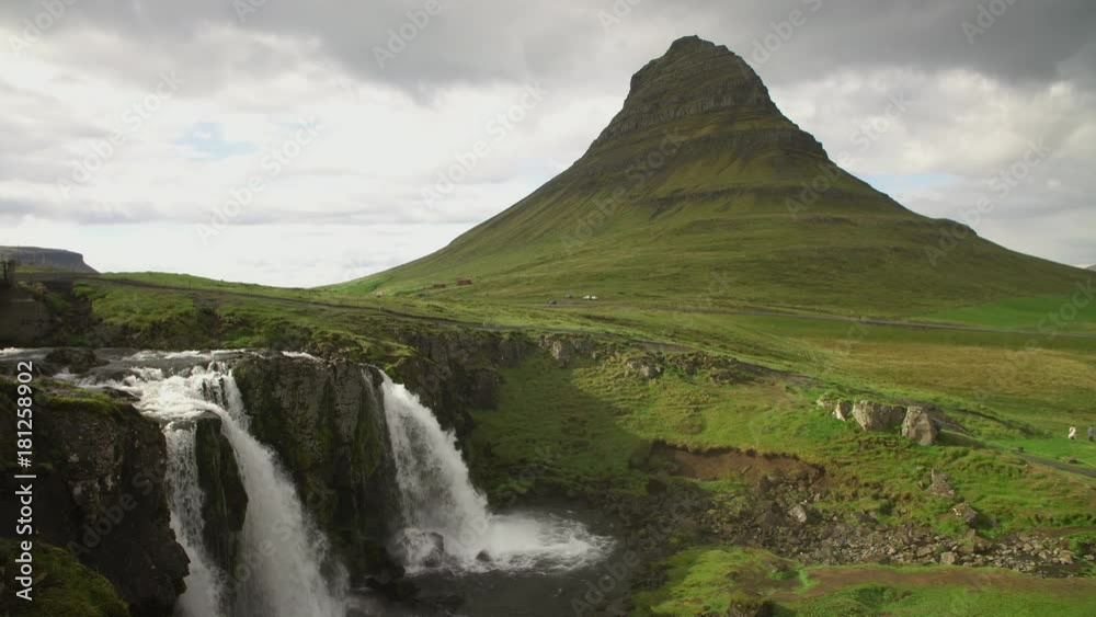 Kirkjufellsfoss waterfall cascades and Kirkjufell mountain and fresh green grass famous touristic point in western region Iceland