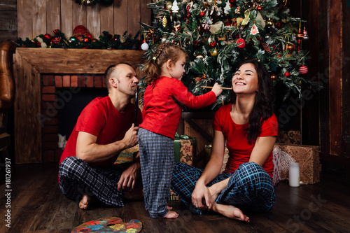 The family in pajamas plays next to a Christmas tree and a fireplace.