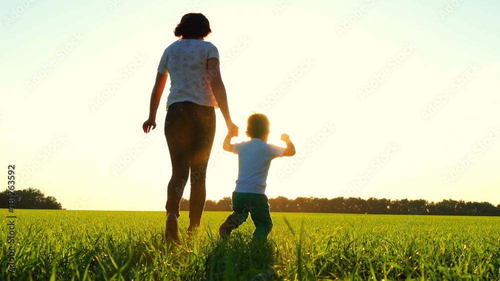 Mother and child are running across the field at sunset (flesh shot) - 1. Mom and her son are running around on a green lawn.