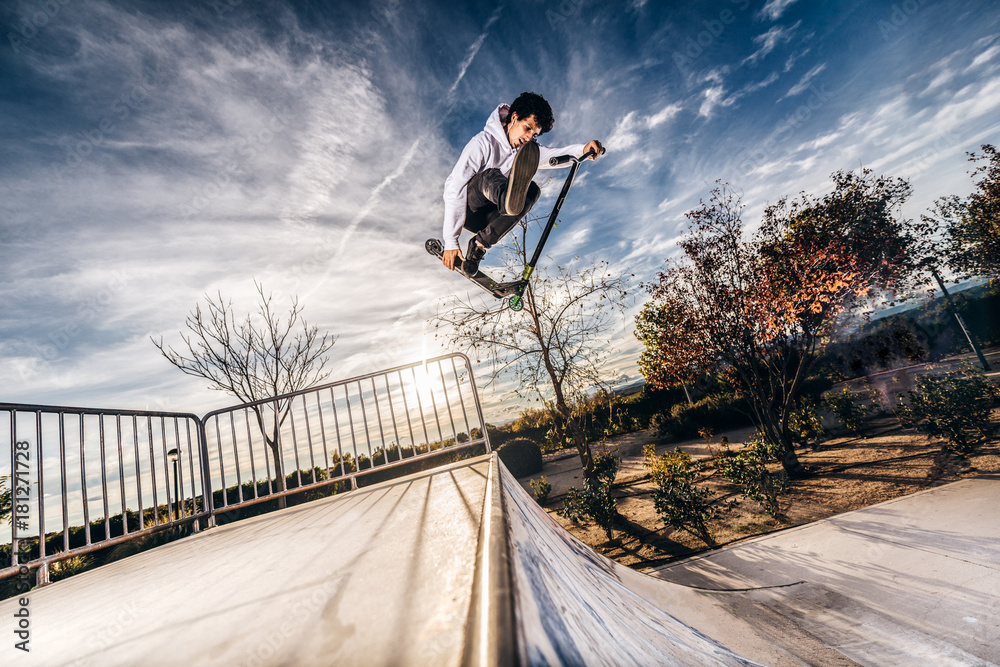 Young man with scooter making a jump on Skatepark during sunset foto de  Stock | Adobe Stock