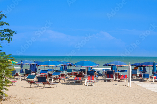 Adriatic Sea coast view. Seashore of Italy  summer umbrellas on sandy beach with clouds on horizon.