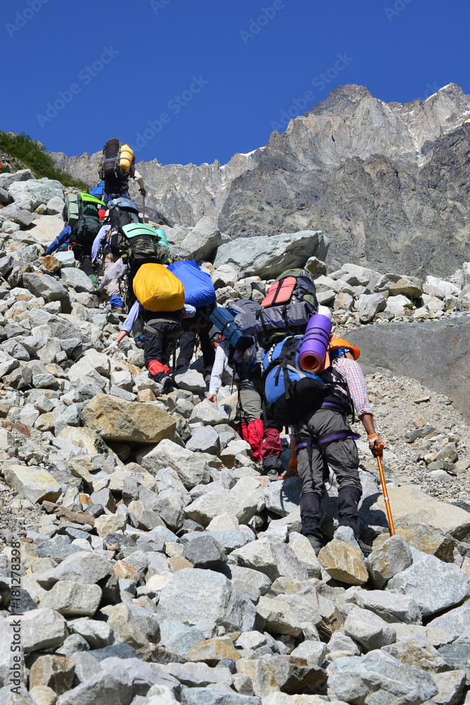 A group of hiking tourists go along the glacier to the mountain pass. The weather facilitates complex movement in the high-mountainous area. Travelling in the Caucasian Mountains in Georgia.