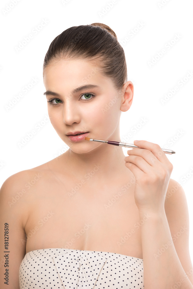 Fototapeta premium Portrait of beautiful young brunette woman with clean face. Beauty spa model girl with perfect fresh clean skin applying cosmetic brush. Youth and skin care concept. Isolated on a white background.