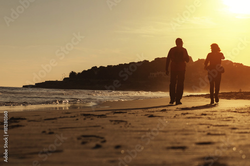 Obraz na plátně Silhouette of couple walking on the beach at sunset