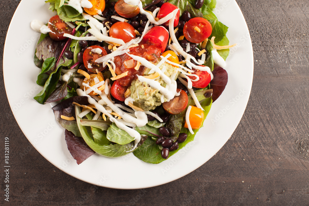 Green spinach salad with chopped red and orange tomato, black beans, shredded cheese, avocado, and salsa on a white plate above shot
Green spinach salad with chopped red and orange tomato, black beans, shredded cheese, avocado, and salsa on a white plate above shot
