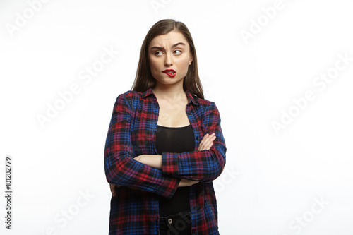 Portrait of emotional doubtful uncertain young brunette female biting lips and posing in studio with arms folded, thinking over some offer, can't make decision, feeling hesitant and puzzled © Anatoliy Karlyuk