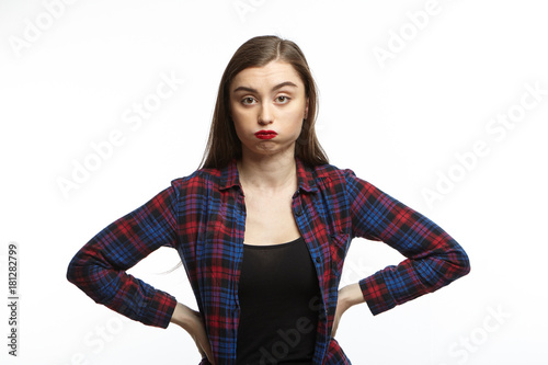 Foto Picture of annoyed young woman wearing plaid shirt over black t-shirt holding hands on her waist and puffing her cheeks, feeling fed up and puzzled with something irritatting
