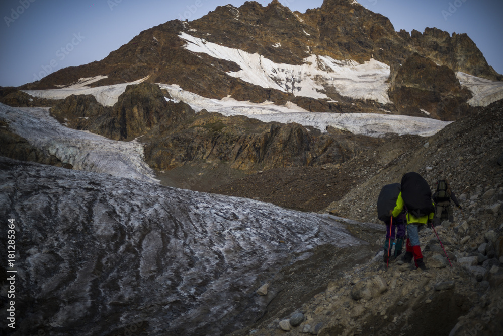Fototapeta premium A group of hiking tourists go along the glacier to the mountain pass. The weather facilitates complex movement in the high-mountainous area. Travelling in the Caucasian Mountains in Georgia