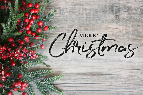 Merry Christmas Text with Christmas Evergreen Branches and Berries in Corner Over Rustic Wooden Background
