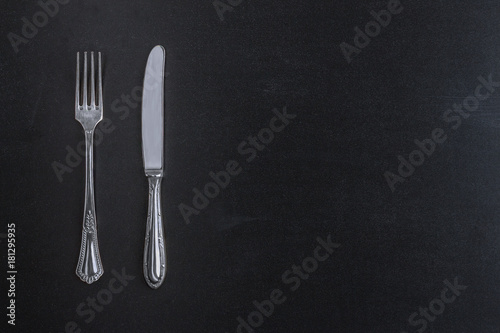 Fork and knife cutlery on black chalkboard background top view top view template for menu